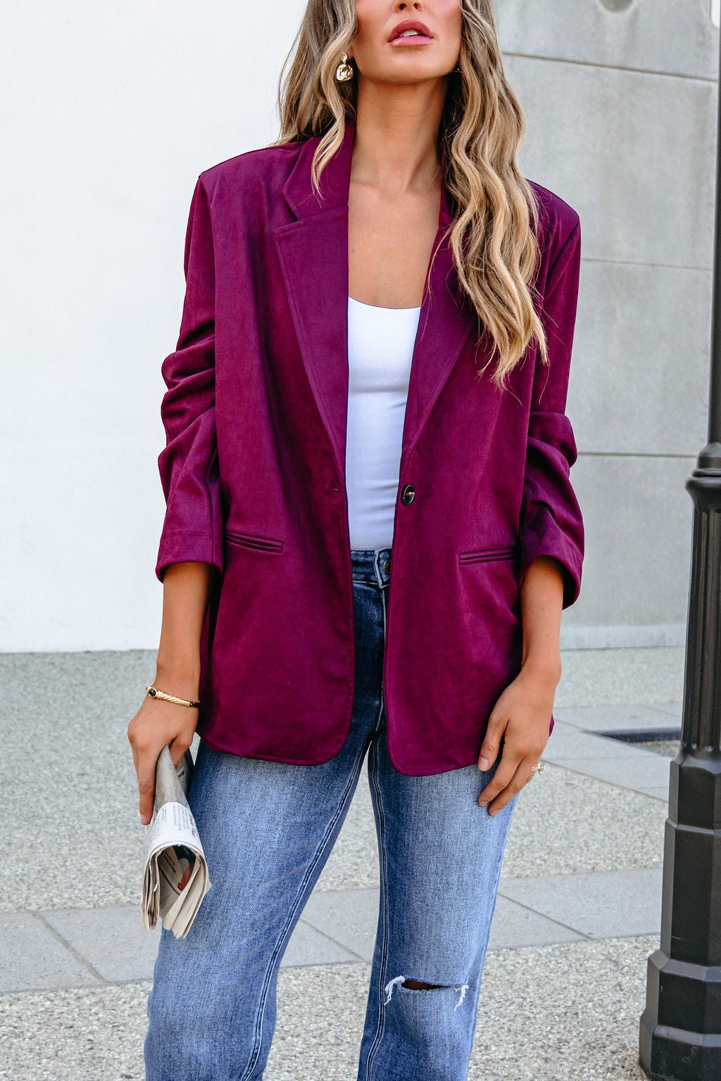 Woman in SHE AND SKY ST1741 Wine Suede Oversized Blazer, white top, and jeans, wavy hair, holding a newspaper outdoors.