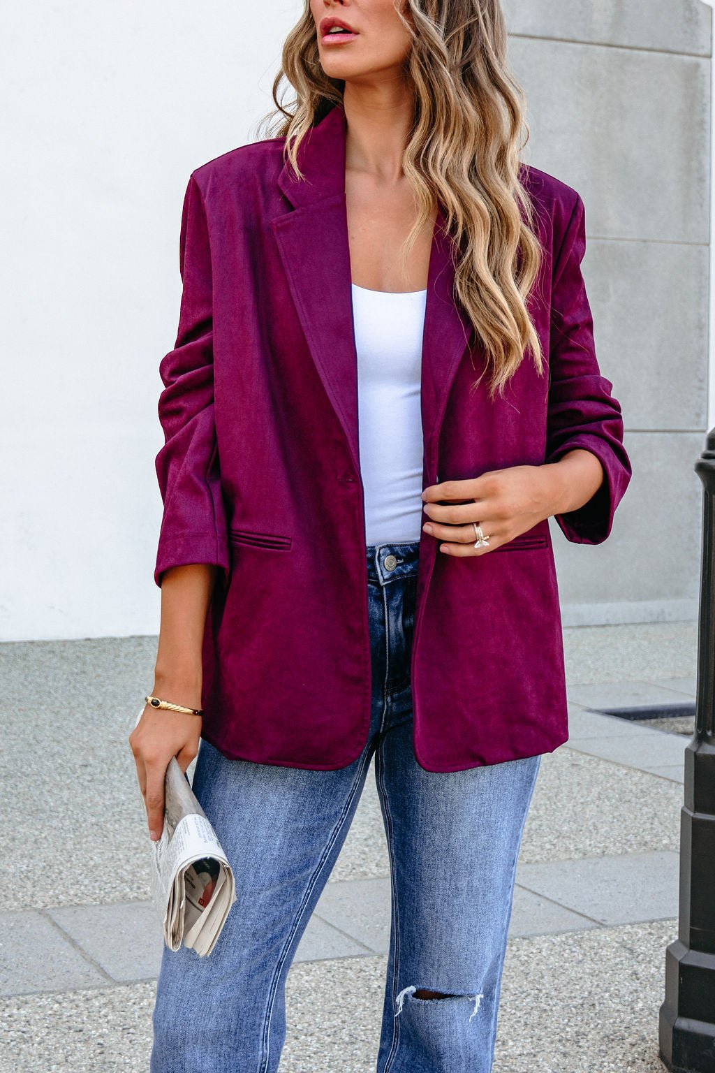 Woman in a SHE AND SKY ST1741 wine suede oversized blazer jacket, white top, and jeans, holding a newspaper outdoors.