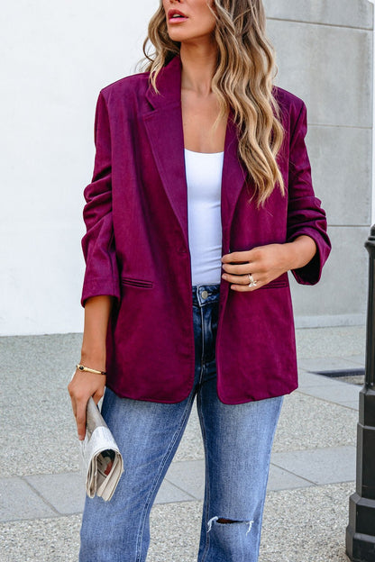Woman in a SHE AND SKY ST1741 wine suede oversized blazer jacket, white top, and jeans, holding a newspaper outdoors.