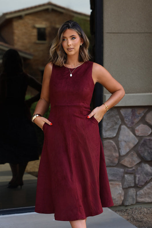 A woman wears a Sleeveless Round Neck Midi Dress - Garnet, featuring a sleeveless silhouette, round neck, and side pockets.