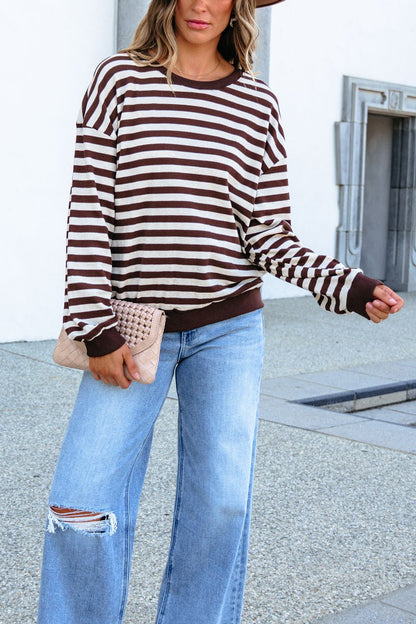 Woman in SHE AND SKY ST1813 brown striped top, blue ripped jeans, holding tan clutch, standing outdoors.