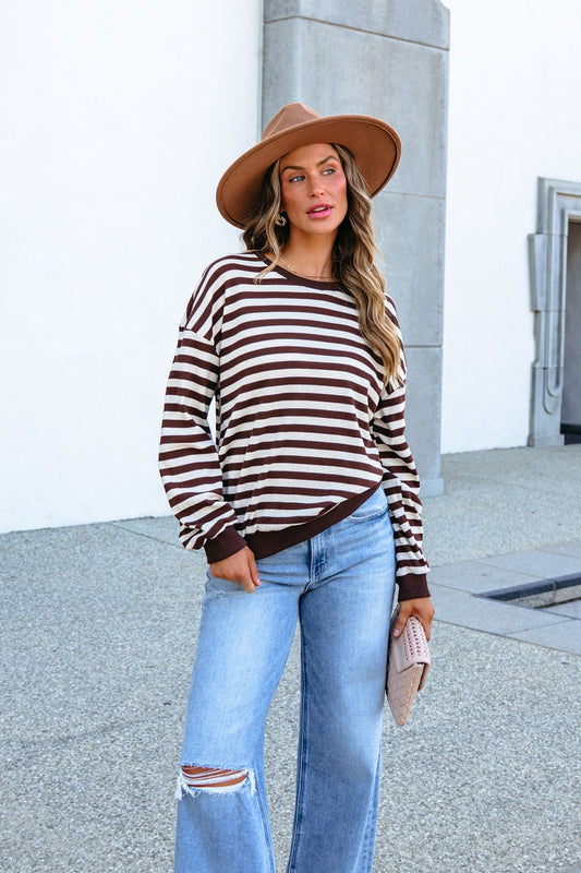 A woman wearing a Long Sleeve Striped Top - Brown, blue jeans, and a brown fedora.