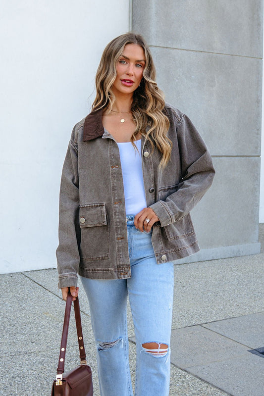 A person wears a brown Twill Barn Jacket with a dark corduroy collar over a white top and ripped light-wash jeans.