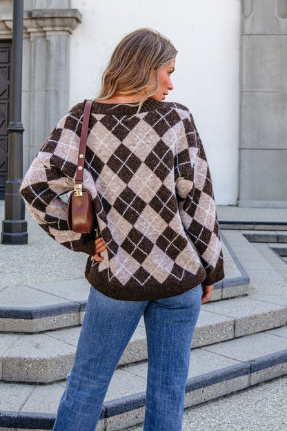Woman with long hair wears the SHE AND SKY ST1999 brown argyle sweater and blue jeans, standing outdoors facing away.