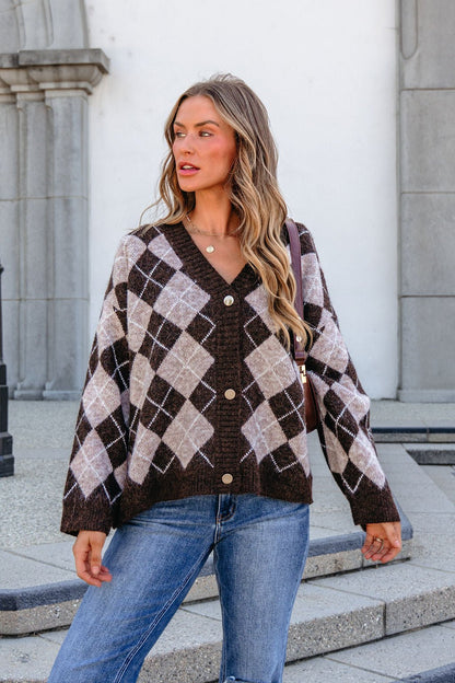 Woman wears the SHE AND SKY ST1999 brown argyle sweater and jeans, standing outdoors by a stone building, looking to the side.