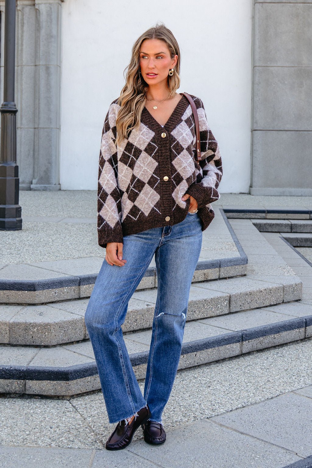 Woman models SHE AND SKY ST1999 brown long sleeve argyle sweater outdoors with blue jeans, dark loafers, and wavy hair.