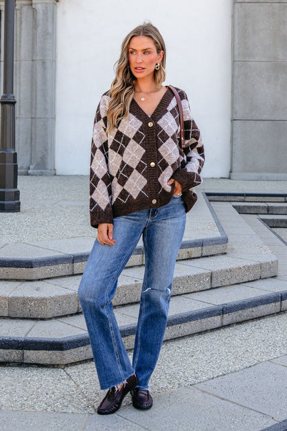 Woman models SHE AND SKY ST1999 brown long sleeve argyle sweater outdoors with blue jeans, dark loafers, and wavy hair.