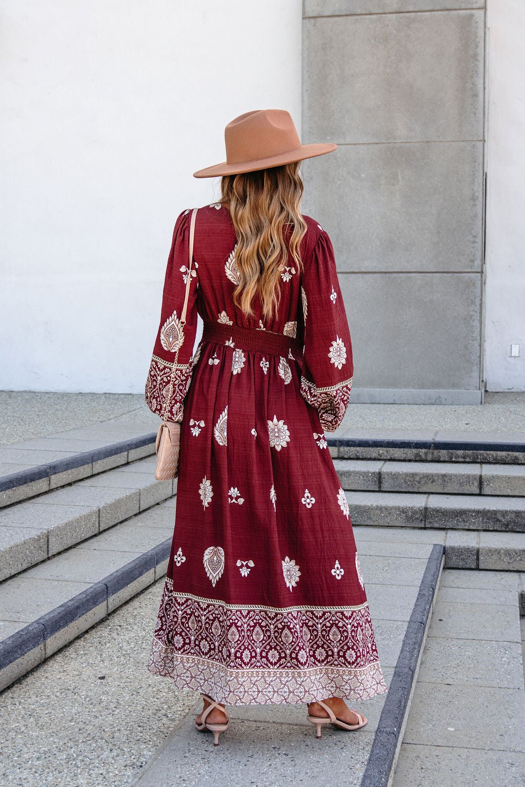 A woman in a SHE AND SKY ST2144 brown printed long sleeve maxi dress stands on outdoor steps, facing away from the camera.