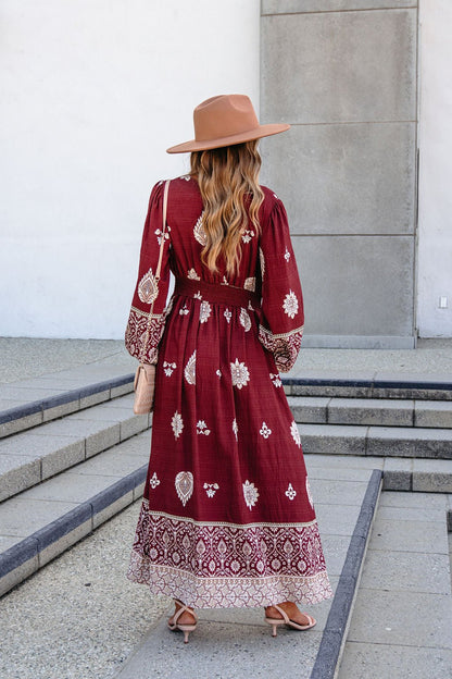 A woman in a SHE AND SKY ST2144 brown printed long sleeve maxi dress stands on outdoor steps, facing away from the camera.