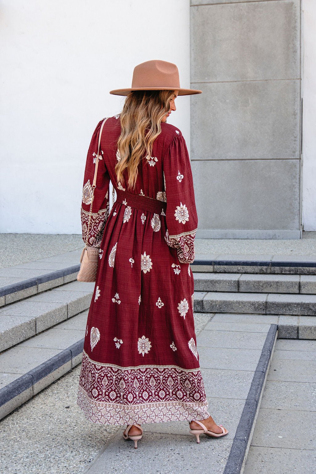 Woman in a SHE AND SKY ST2144 brown printed long sleeve maxi dress stands outdoors, facing away from the camera.