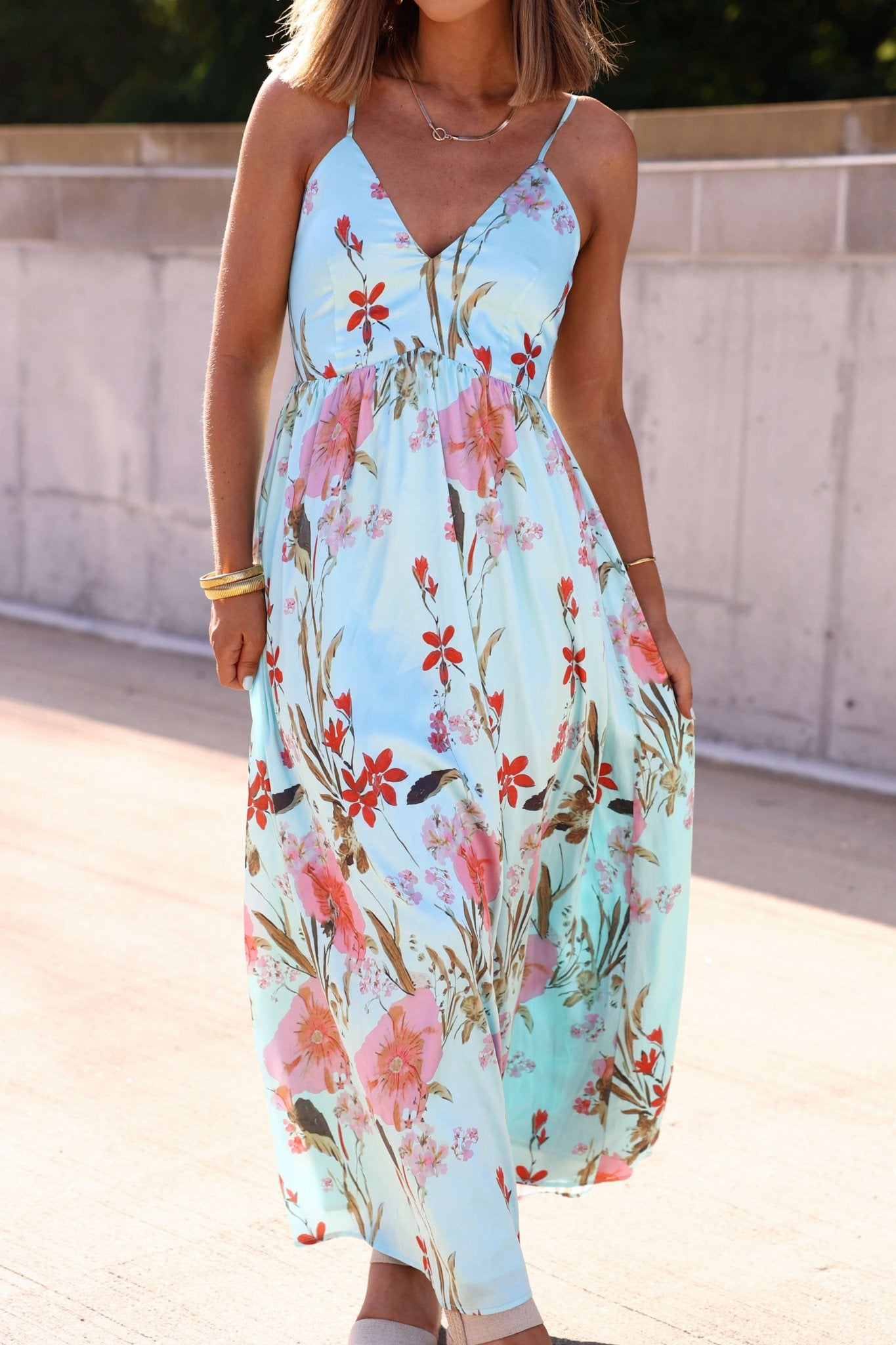 Woman in a Silky Blue Multi Floral Print Maxi Dress with thin straps, walking outdoors on a sunny day.