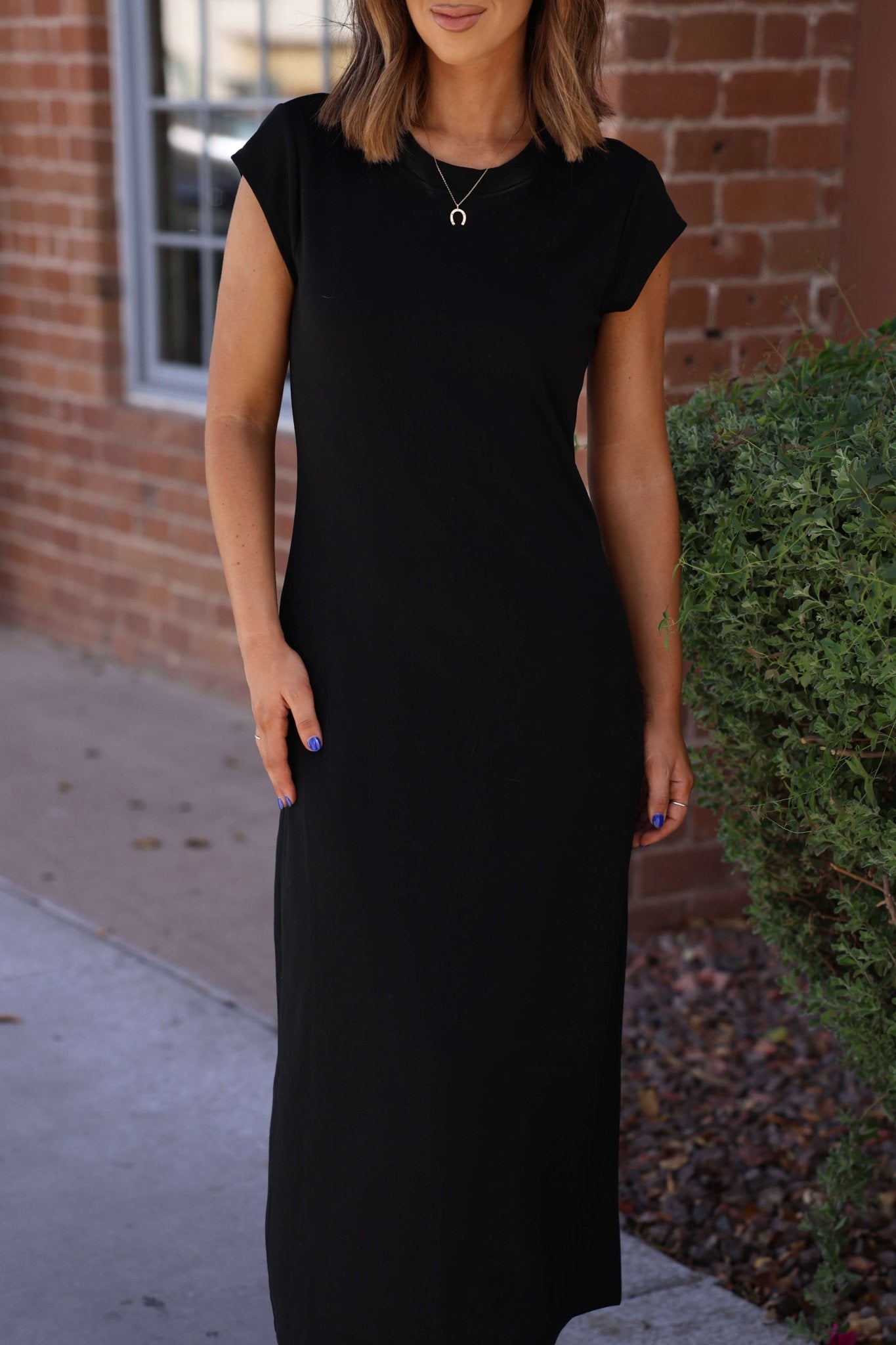A woman stands outside in the Simple Timeless Black Midi Dress - FINAL SALE, a classic wardrobe essential.