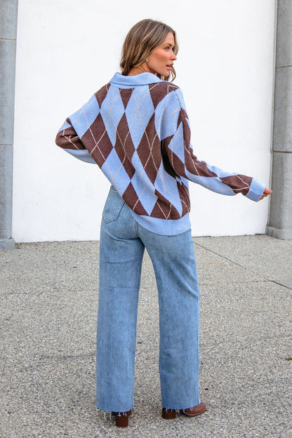 Someone in the Sky Blue Argyle Ribbed Sweater and light blue jeans stands outdoors facing away from the camera.