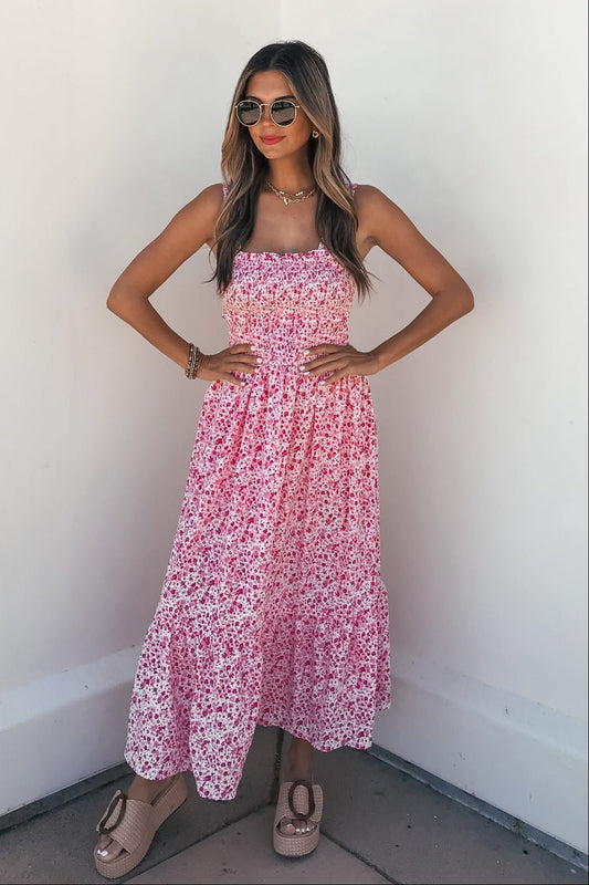 Woman in sunglasses wears the Smocked Bow Tie Print Midi Dress - Pink with platform sandals, standing against a white wall.