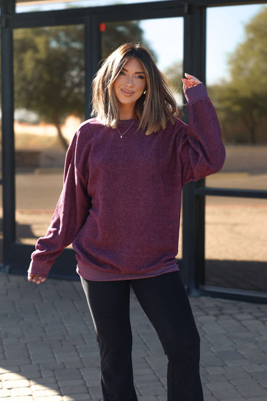 Woman with shoulder-length hair smiles outdoors in a plum Soft Brushed Oversized Sweatshirt and black pants.