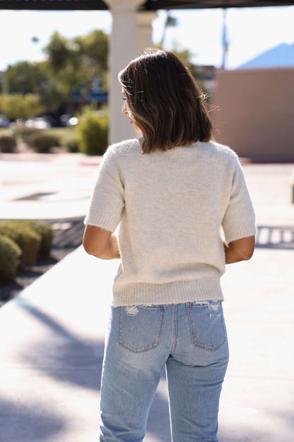 A woman in the Soft & Comfy Oatmeal Sweater - FINAL SALE and light blue jeans stands outdoors, facing away.