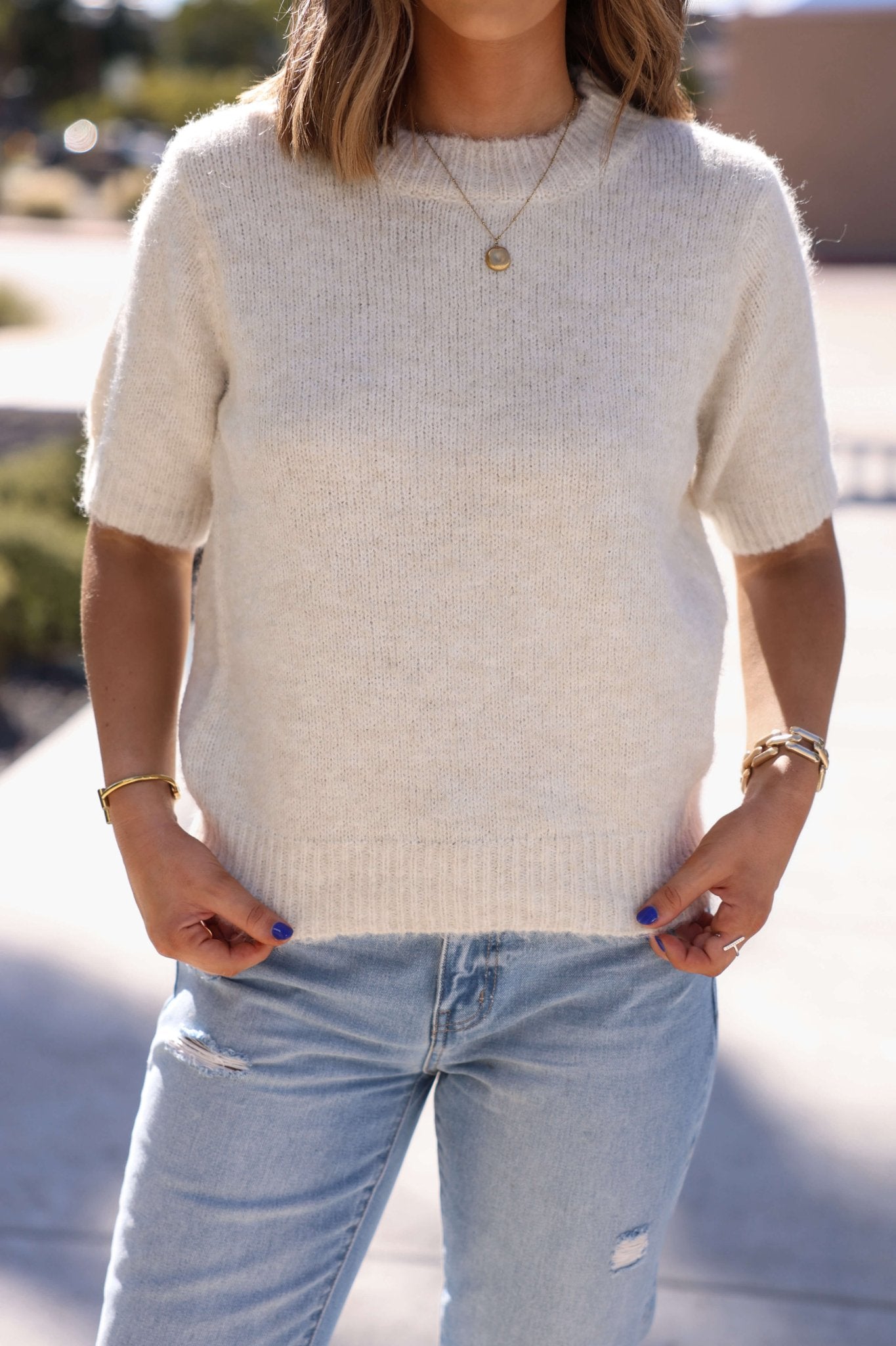 Woman in the Soft & Comfy Oatmeal Sweater - FINAL SALE, with light blue ripped jeans and gold jewelry, standing outdoors.