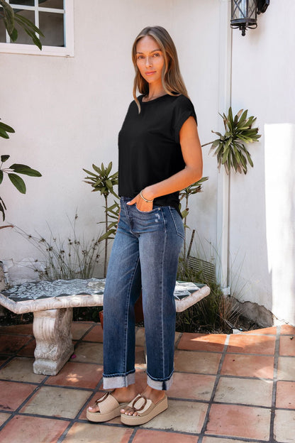 Woman standing on a tiled patio in a relaxed fit Soft Modal Basic Tee - Black, cuffed jeans, and platform sandals near plants.