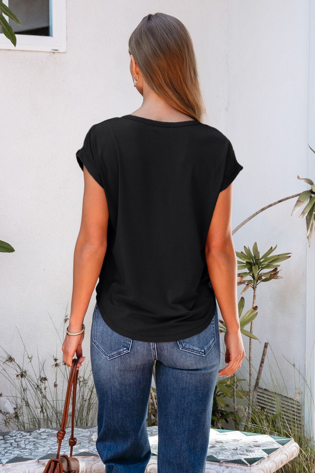 A woman in a relaxed fit Soft Modal Basic Tee - Black and blue jeans stands outdoors, holding a brown bag by her side.