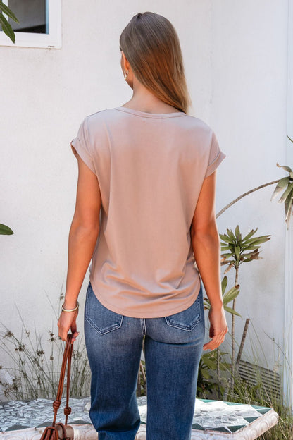 A woman with long hair wears the Soft Modal Basic Tee - Mocha and blue jeans, standing outdoors among plants, facing away.
