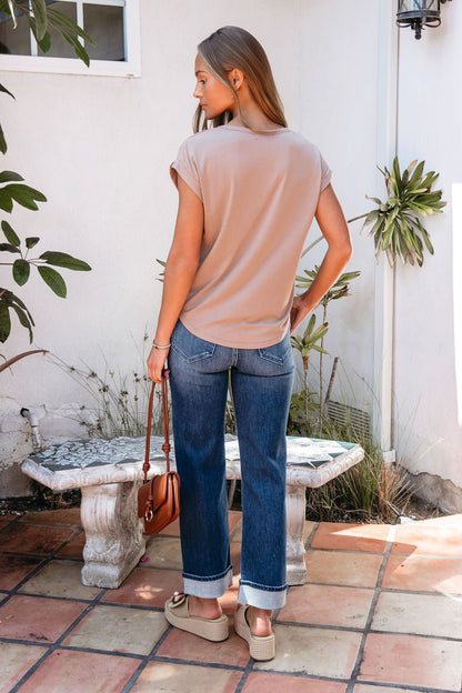 A woman in a relaxed fit Soft Modal Basic Tee - Mocha, blue cuffed jeans, and sandals stands outside with a brown purse, back to camera.