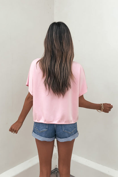 A woman with long wavy hair wears a Soft Cloud Scuba Lounge Top in pink, standing with her back to the camera by a white wall.