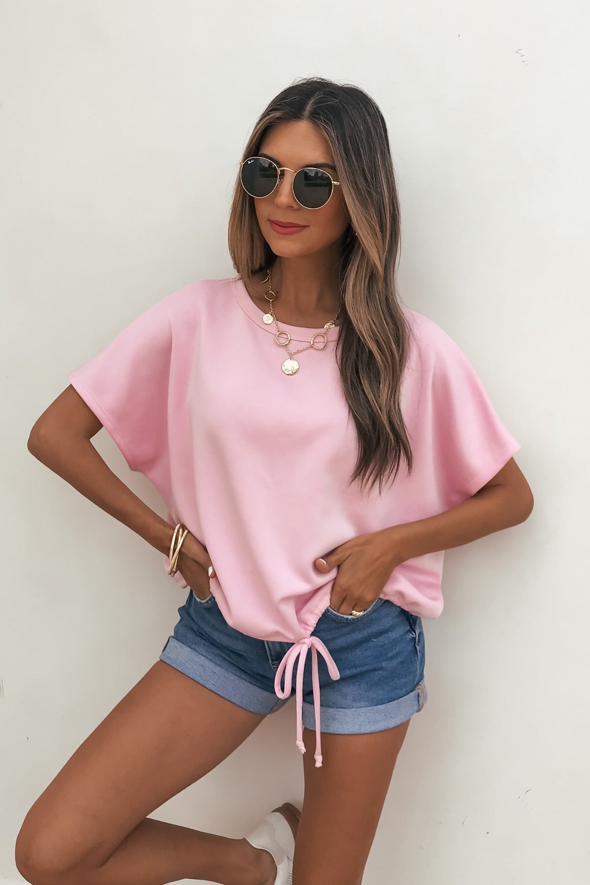 Woman in sunglasses, Soft Cloud Scuba Lounge Top - Pink, denim shorts, and jewelry stands against a white wall.