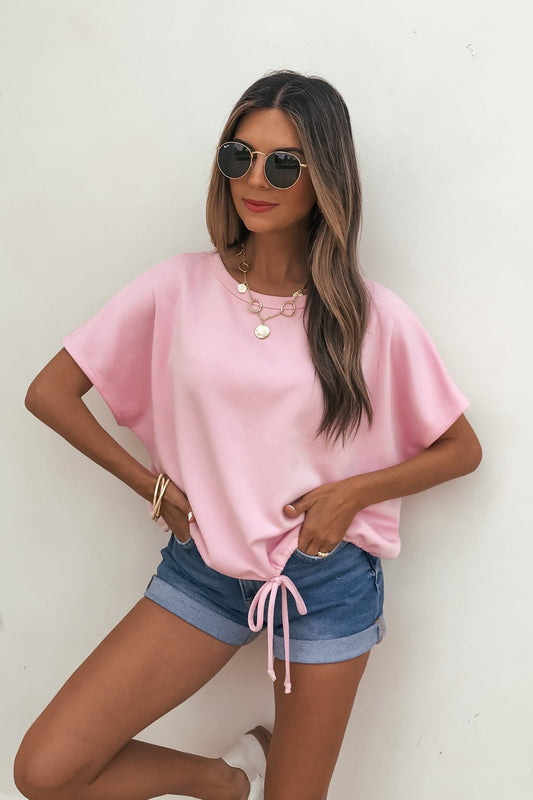 Woman in sunglasses in a relaxed fit Soft Scuba Lounge Top - Pink, denim shorts, and gold jewelry against a plain white background.