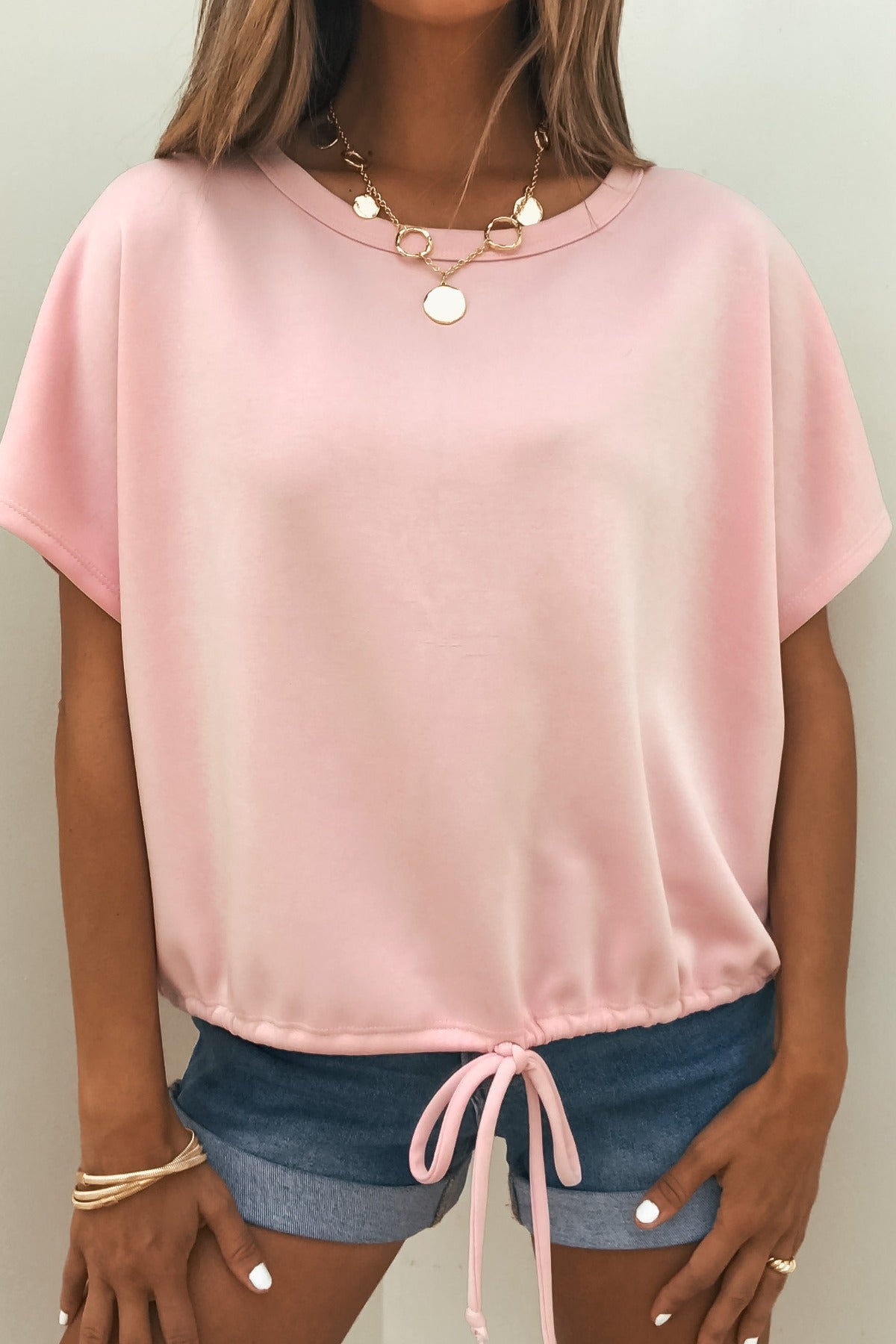 Woman in a Soft Cloud Scuba Lounge Top - Pink, paired with blue denim shorts, gold necklace, and bracelets.
