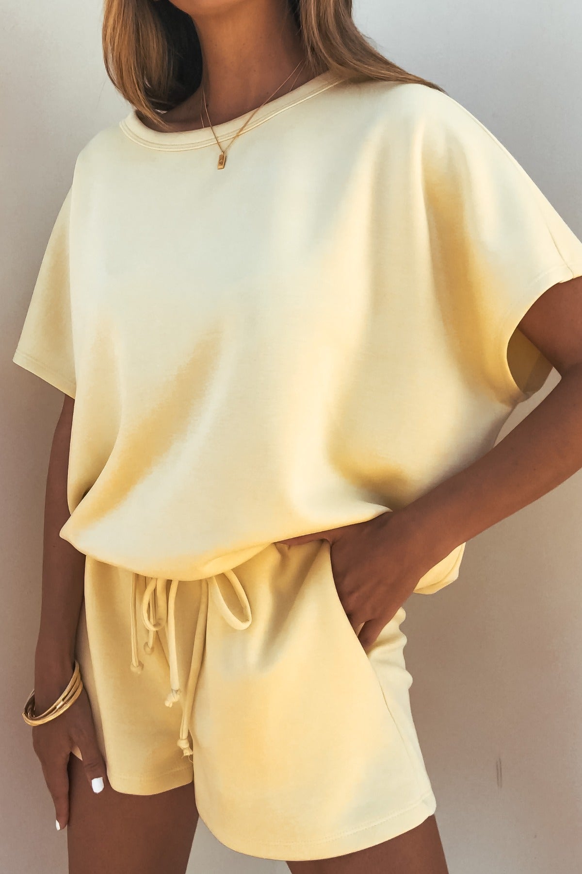 Woman in a relaxed fit Soft Cloud Scuba Lounge Top - Yellow and matching drawstring shorts, accessorized with bracelets and a necklace.