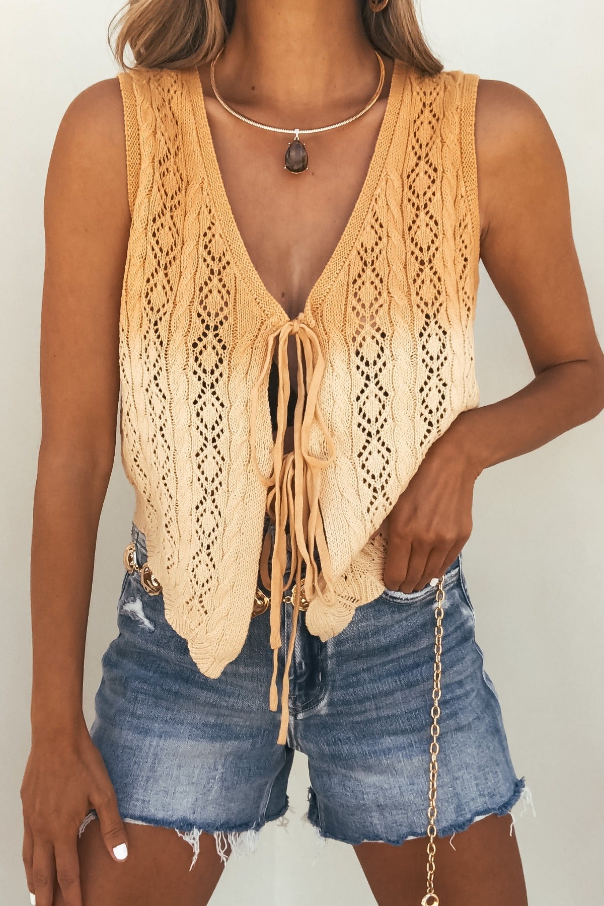 Woman wears a Solstice Ombre Crochet Tie‑Front Top, denim shorts, chain belt, and a stone pendant necklace.