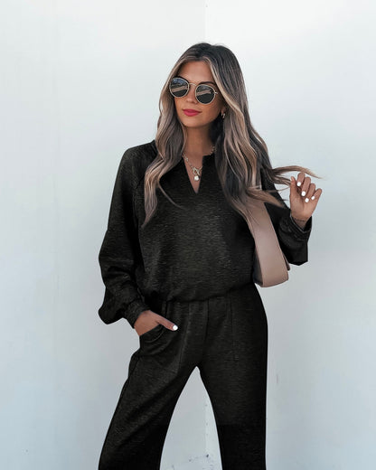 Woman with long wavy hair wears sunglasses, necklaces, and Stay Active Black Lounge Sweatpants against a plain white background.