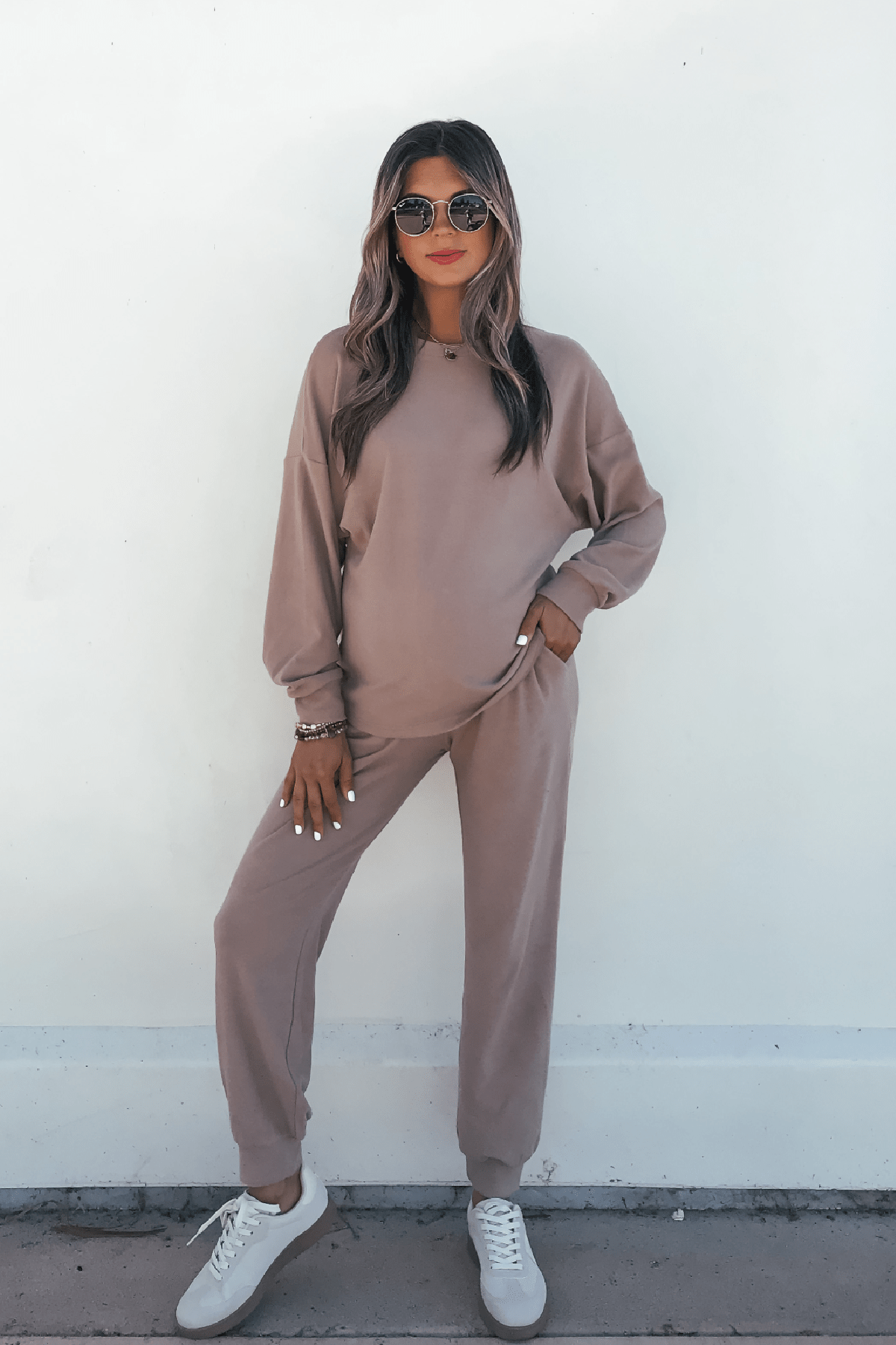 A person wearing a mocha Step Up Lounge Set with a long-sleeved pullover and joggers, styled with white sneakers and sunglasses.