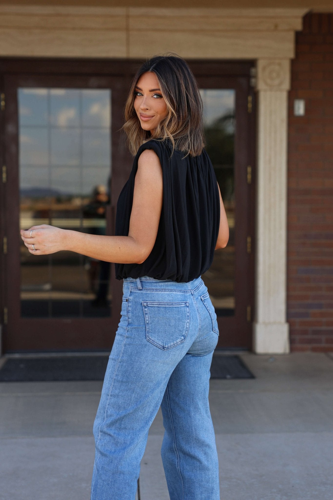 Woman with shoulder-length hair models the Steve Madden Black Cherra Mesh Top and blue jeans outdoors, looking over her shoulder.