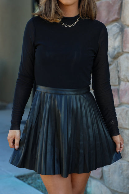 A woman in a Steve Madden Black Nevah Mini Dress stands by a stone wall, exuding effortless style and sophistication.