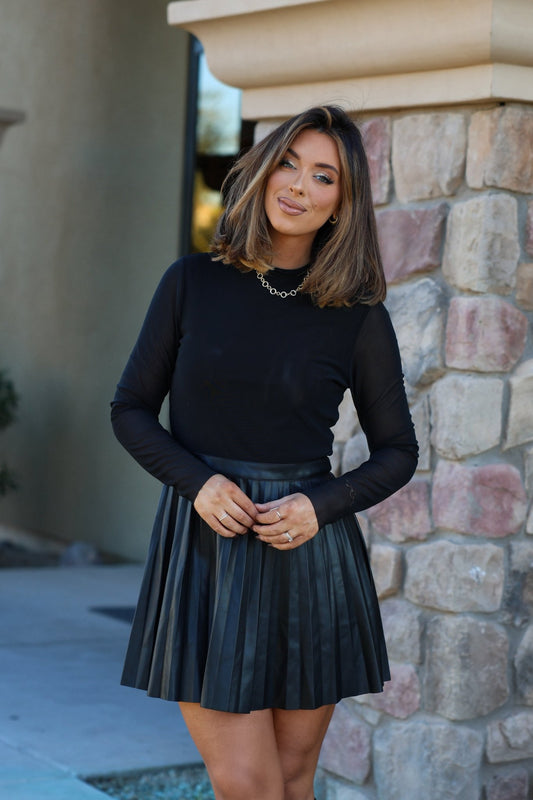 A woman in a Steve Madden Black Nevah Mini Dress smiles at the camera while standing in front of a stone wall.