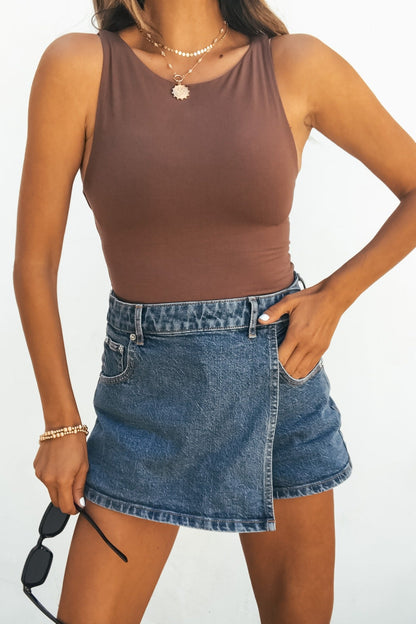 Woman in a brown sleeveless top and Steve Madden Brightin Skort - Medium Wash, holding sunglasses with one hand in her pocket.