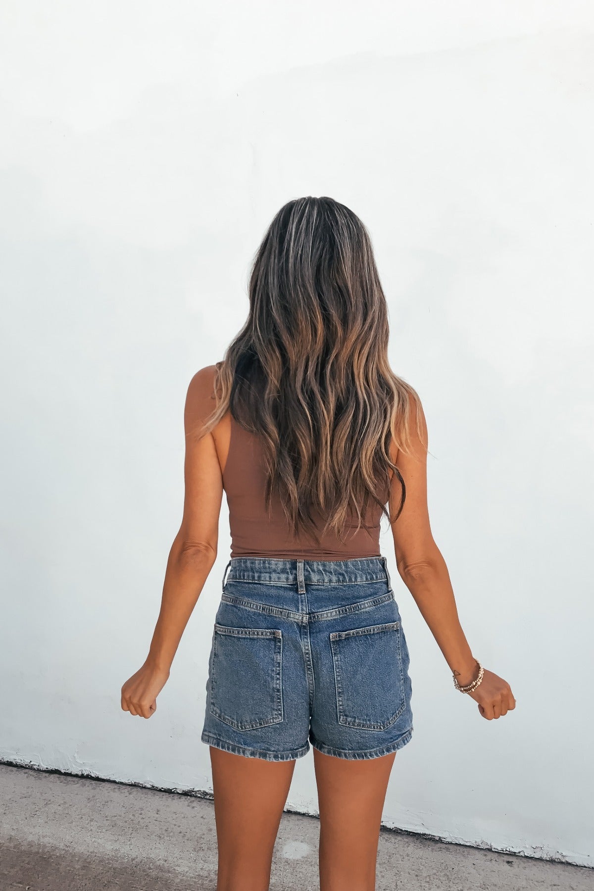 Woman with long wavy hair wears a brown tank and Steve Madden Brightin Skort - Medium Wash, standing before a plain white wall.