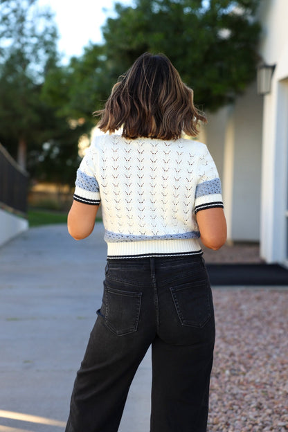 A woman with shoulder-length hair stands outside wearing the Steve Madden Cream Fiona Sweater Cardigan and black jeans.