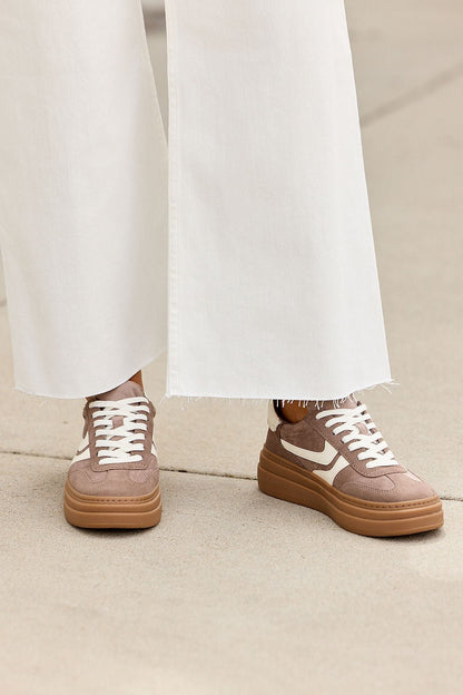 Person in wide-legged white pants and Steve Madden Dodge Sneakers - Taupe, standing on a light concrete surface.