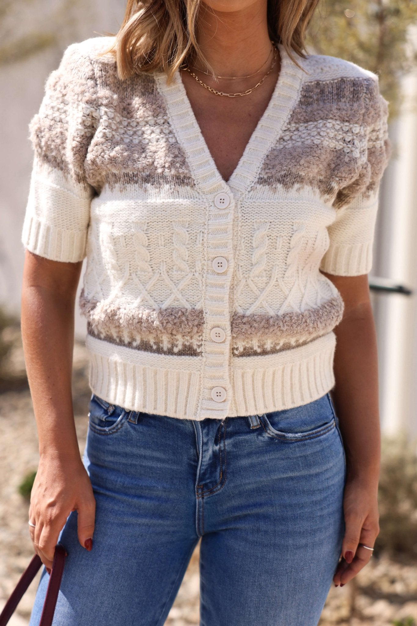 Woman outdoors in blue jeans and a Steve Madden Janae Cream Multi Sweater Cardigan with short sleeves.