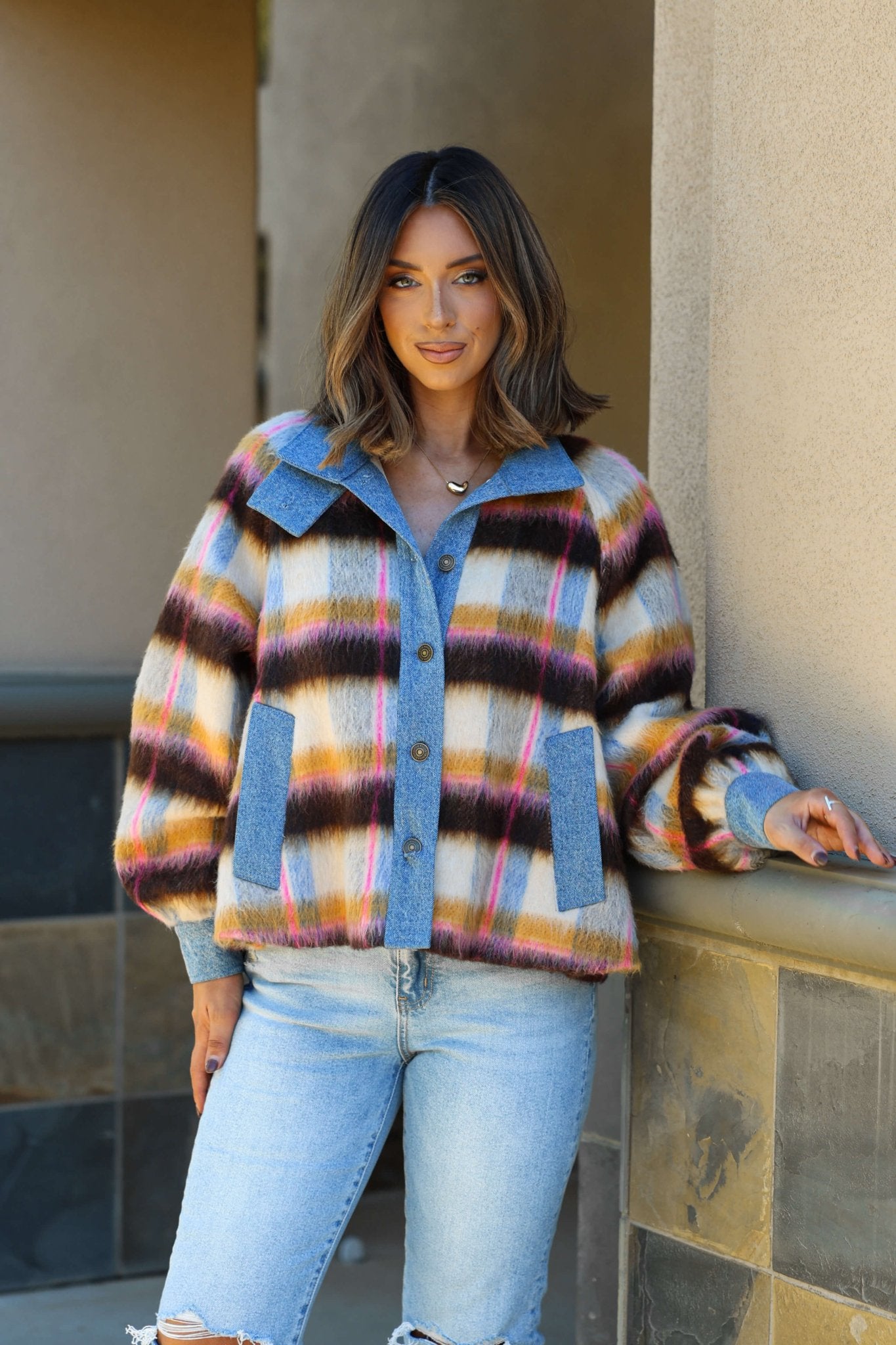 A woman smiles at the camera in a relaxed fit Steve Madden Kaylen Multi Striped Jacket and light blue jeans.