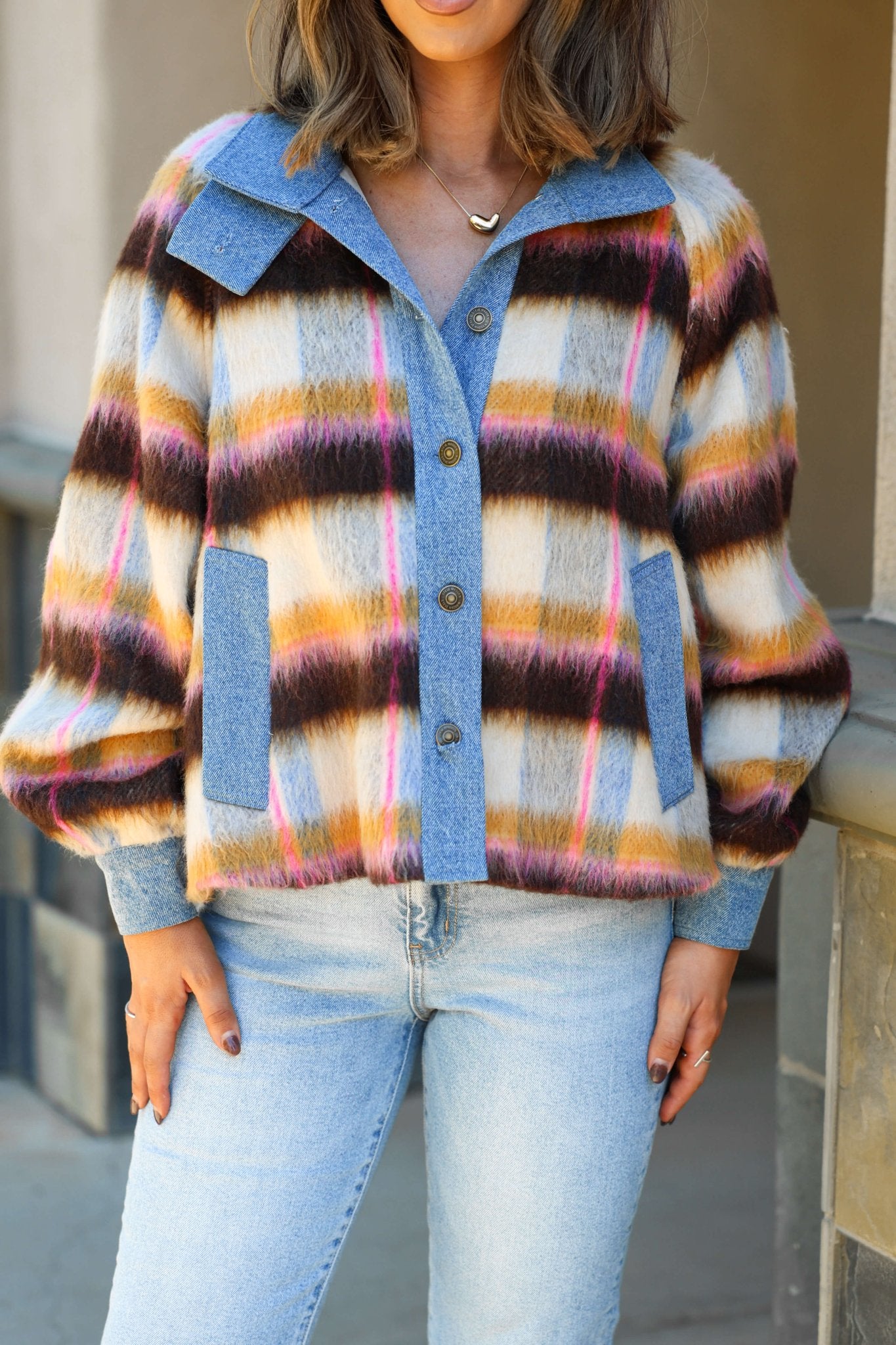 A woman wears the Steve Madden Kaylen Multi Striped Jacket and light blue jeans, standing outside in transitional weather.