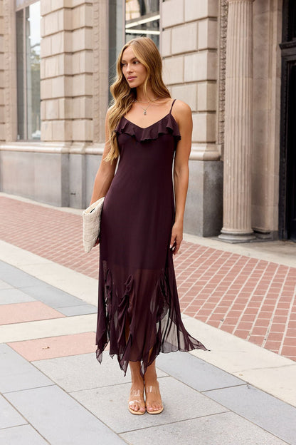 Woman in a sleeveless Steve Madden Mariane Midi Dress - Brown, holding a clutch, stands on a city sidewalk by a stone building.