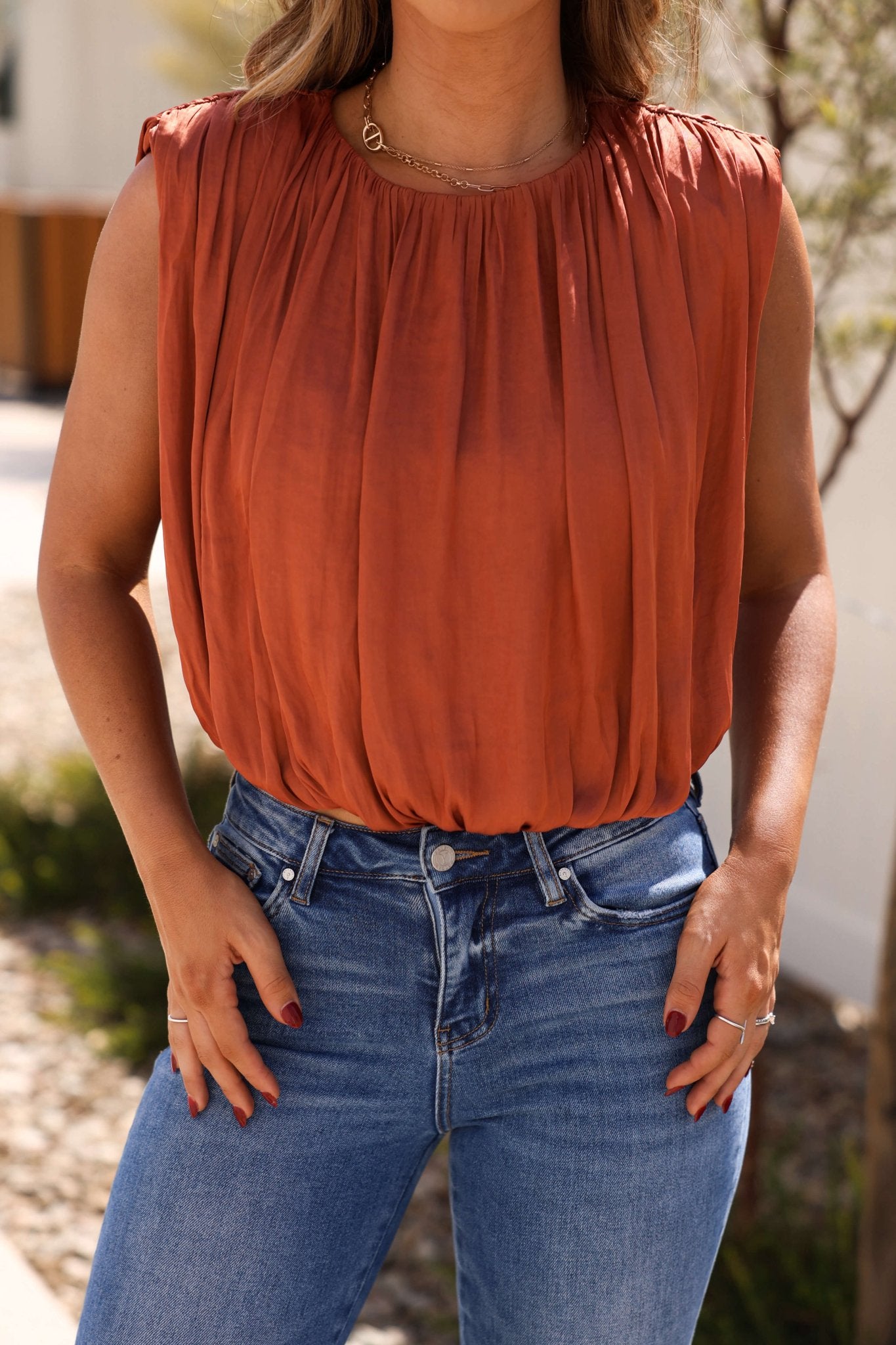 A woman stands outdoors in the Steve Madden Milana Copper Pleated Top, hands on hips, flaunting its chic bubble silhouette.
