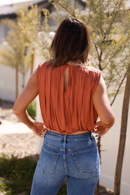 A woman stands outdoors in the Steve Madden Milana Copper Pleated Top, her back to the camera.