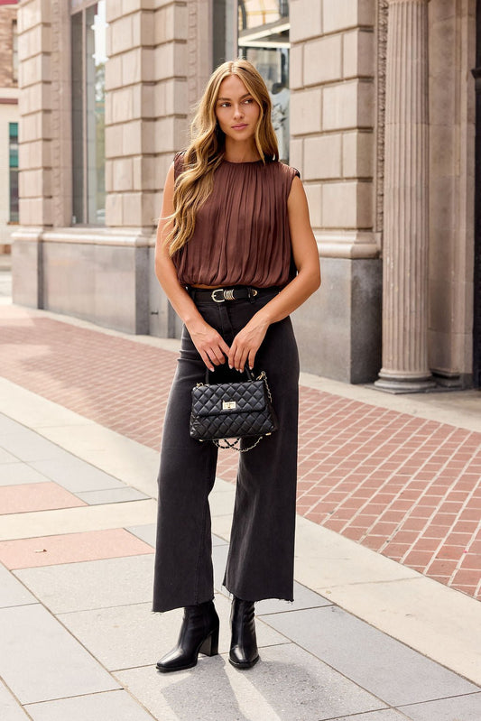 Woman in a brown Steve Madden Milana Top, black wide-leg pants, and boots stands on a city sidewalk with a quilted handbag.