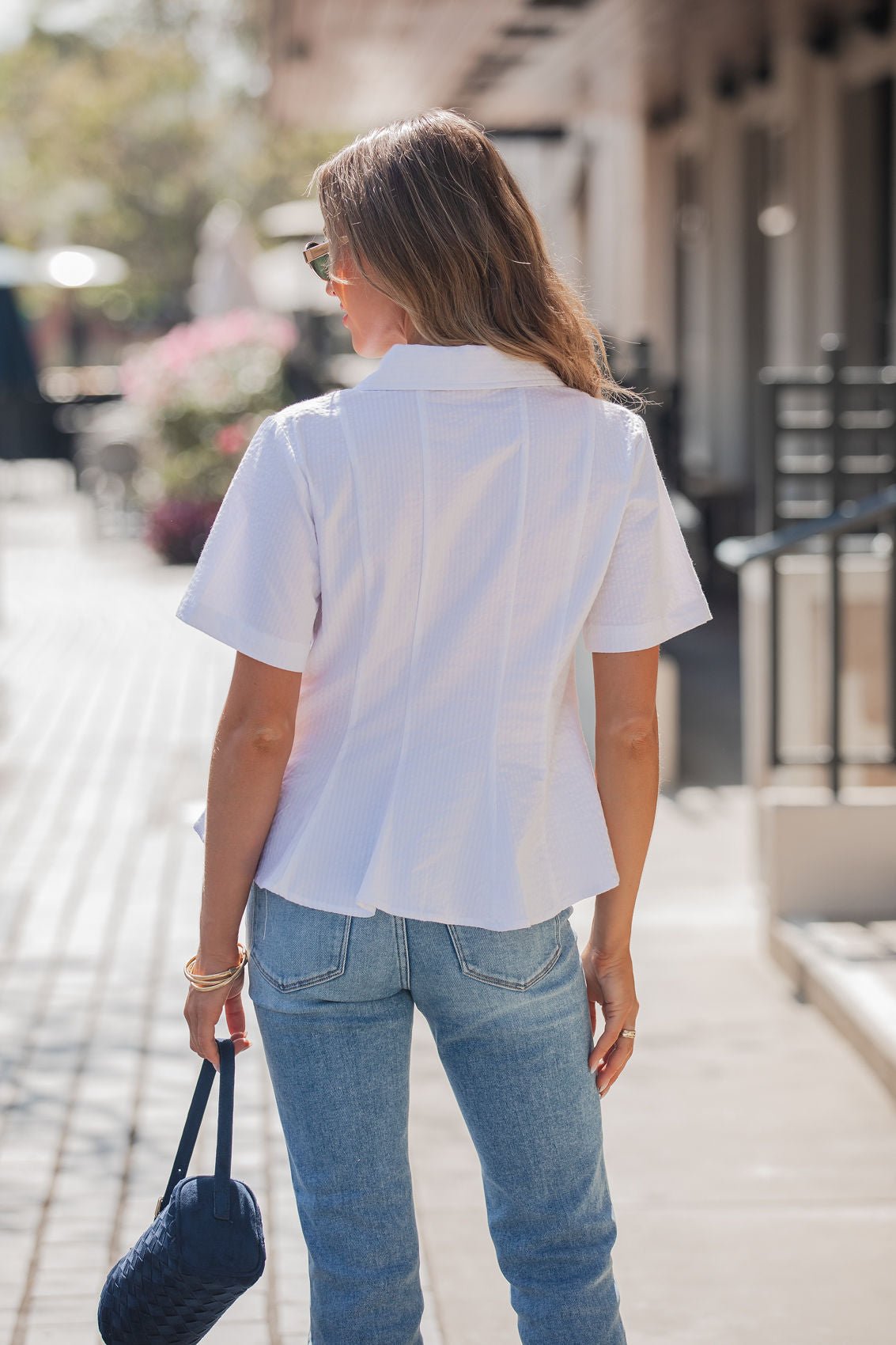 A woman with long hair wears the Steve Madden White Porter Top outdoors, holding a navy purse and facing away from the camera.