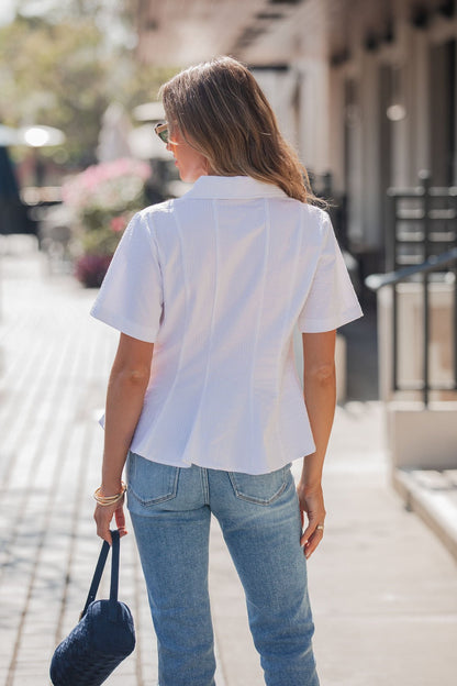 A woman with long hair wears the Steve Madden White Porter Top outdoors, holding a navy purse and facing away from the camera.