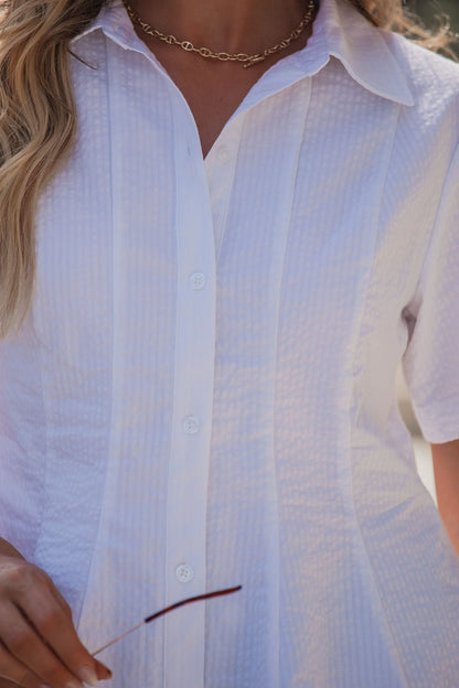 A woman in the Steve Madden White Porter Top - FINAL SALE holds sunglasses and wears a gold chain necklace.
